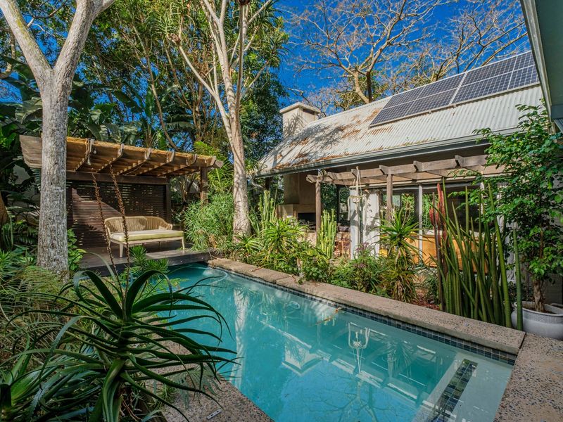 A private outdoor pool area featuring a timber pergola, built-in fireplace, and lush garden surroundings, complemented by solar panels on the roof.