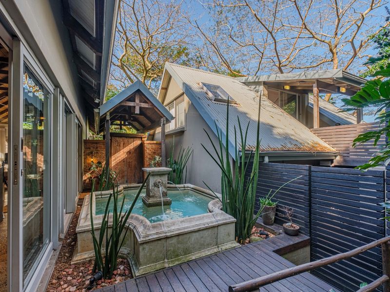 A tranquil outdoor courtyard featuring a stone water fountain, timber decking, and privacy screening, adjacent to the main living area with sliding glass doors.
