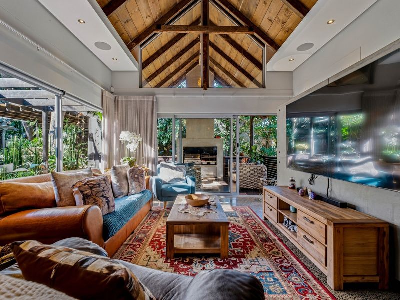 Spacious living room featuring a high vaulted timber ceiling with exposed trusses, recessed lighting, and large sliding glass doors opening to an outdoor patio.
