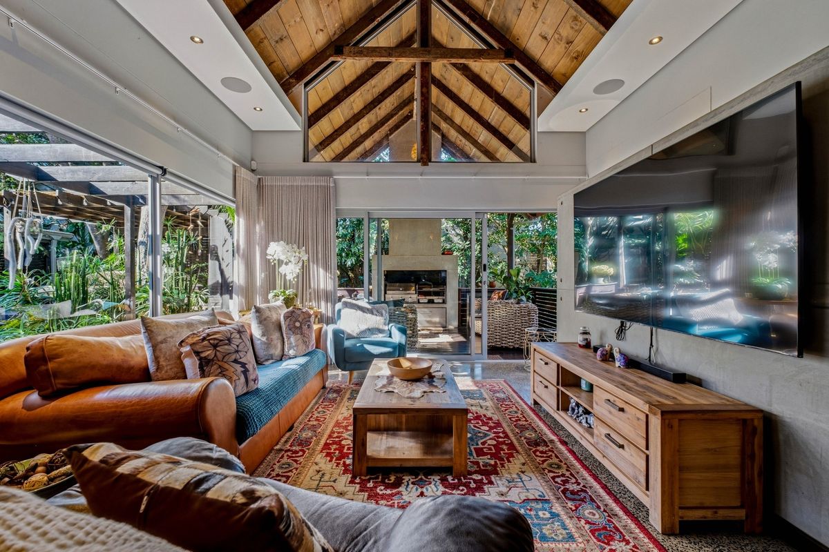 Spacious living room featuring a high vaulted timber ceiling with exposed trusses, recessed lighting, and large sliding glass doors opening to an outdoor patio.