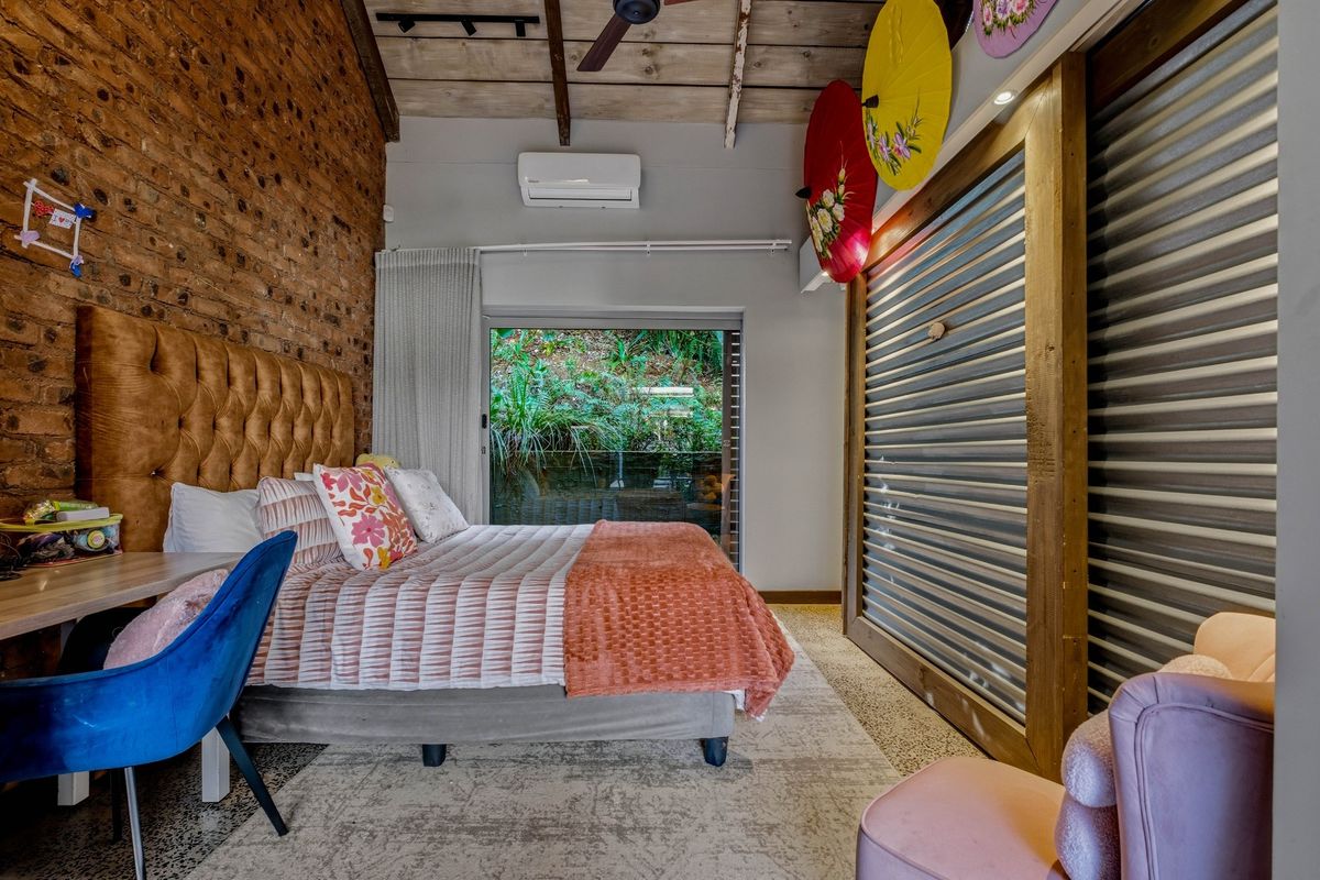 A well-maintained bedroom featuring exposed brickwork, timber ceiling beams, polished concrete floors, and a built-in sliding door wardrobe with direct outdoor access.