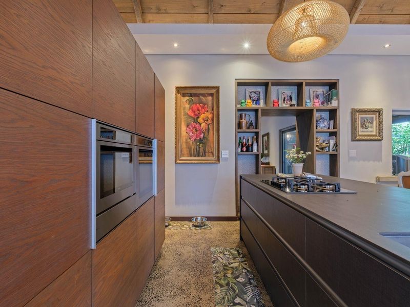 Modern kitchen featuring dark wood cabinetry, a central island with a gas hob, built-in appliances, and exposed timber ceiling beams.