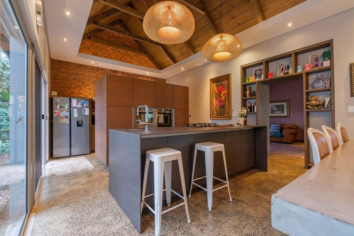 Modern kitchen featuring a large island, polished concrete floors, exposed brick walls, and a vaulted timber ceiling with integrated appliances and ample storage.