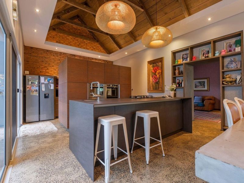 Modern kitchen featuring a large island, polished concrete floors, exposed brick walls, and a vaulted timber ceiling with integrated appliances and ample storage.