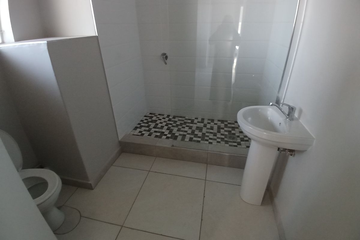 A clean, functional bathroom featuring a pedestal basin, a walk-in shower with a glass screen, and modern mosaic floor tiling.