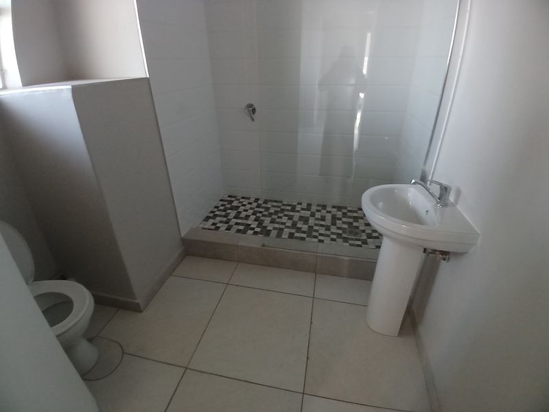 A clean, functional bathroom featuring a pedestal basin, a walk-in shower with a glass screen, and modern mosaic floor tiling.
