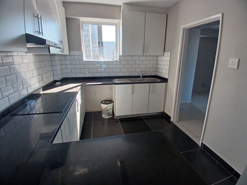 A modern, clean kitchen featuring white cabinetry, dark stone countertops, and a classic subway tile backsplash with ample natural light.