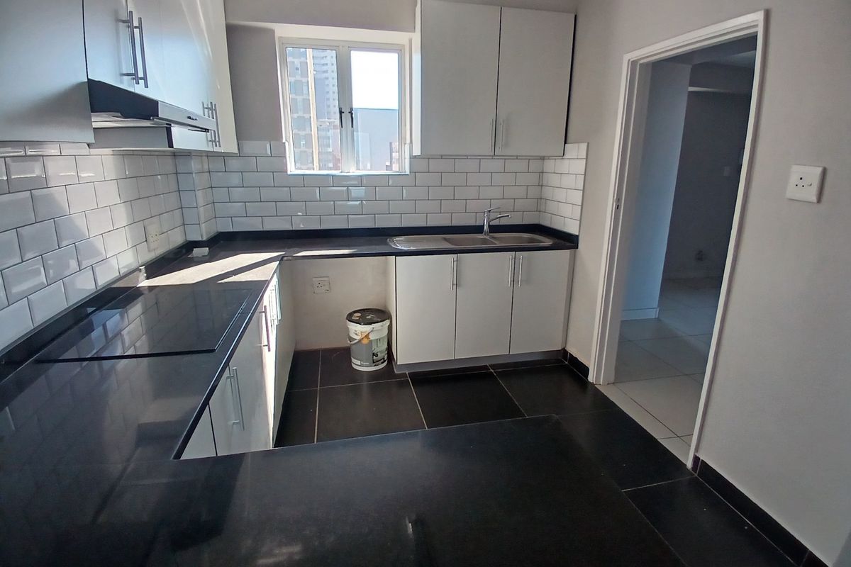 A modern, clean kitchen featuring white cabinetry, dark stone countertops, and a classic subway tile backsplash with ample natural light.