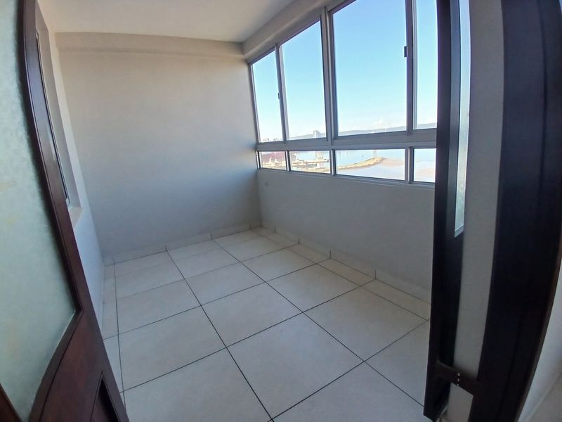 An empty, enclosed balcony featuring tiled flooring and large aluminum-framed windows offering an expansive exterior view.