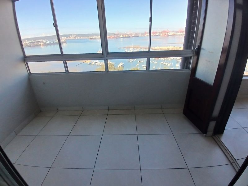 An empty, tiled balcony featuring large sliding glass windows that offer expansive views of the harbor and marina.