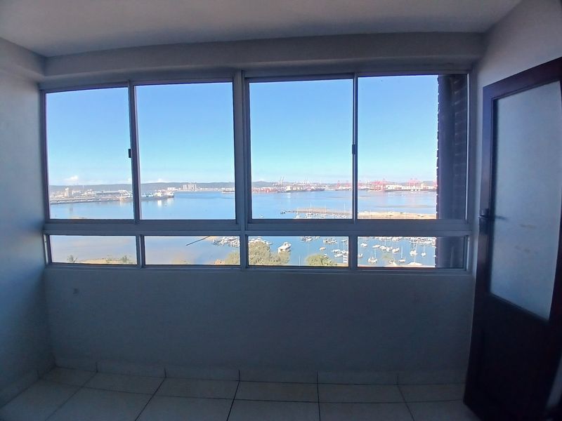 An enclosed balcony featuring tiled flooring and large aluminium windows offering expansive harbour and marina views.
