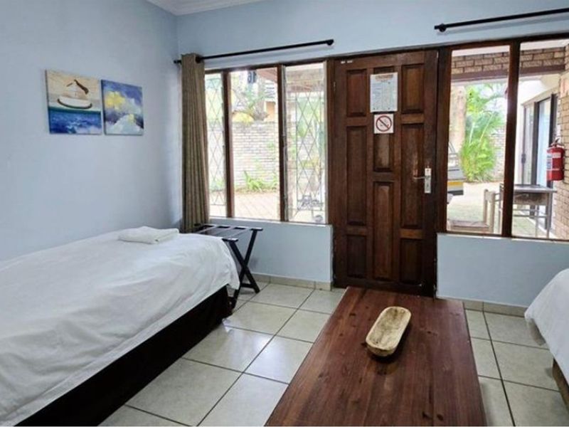 A bedroom featuring tiled flooring, large windows providing natural light, and direct access to an outdoor area through a timber door.