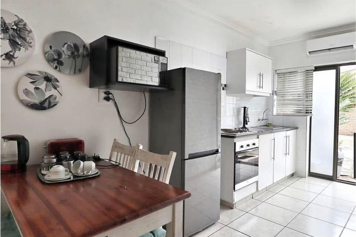 Compact kitchen featuring white cabinetry, tiled backsplash, built-in oven, and hob, with direct access to an outdoor area.