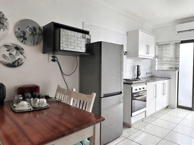 Compact kitchen featuring white cabinetry, tiled backsplash, built-in oven, and hob, with direct access to an outdoor area.