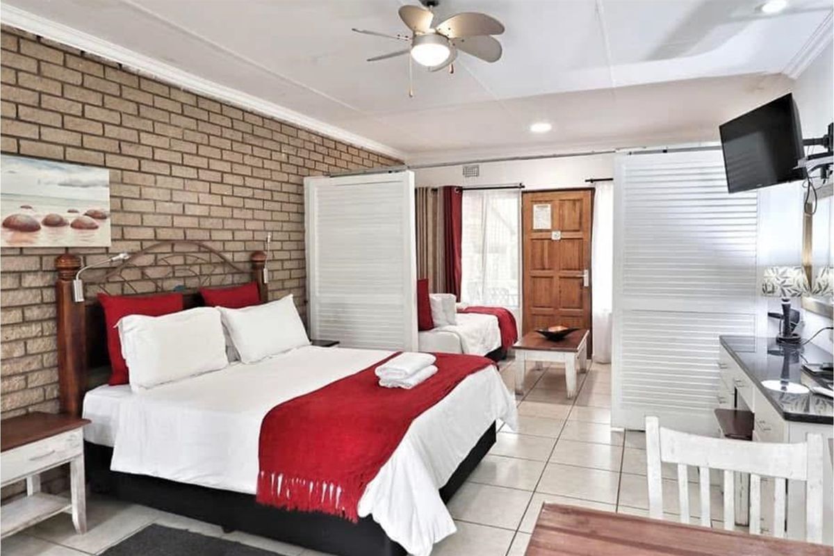 Spacious bedroom featuring an exposed brick feature wall, tiled flooring, and a ceiling fan, with a functional layout and integrated room divider.