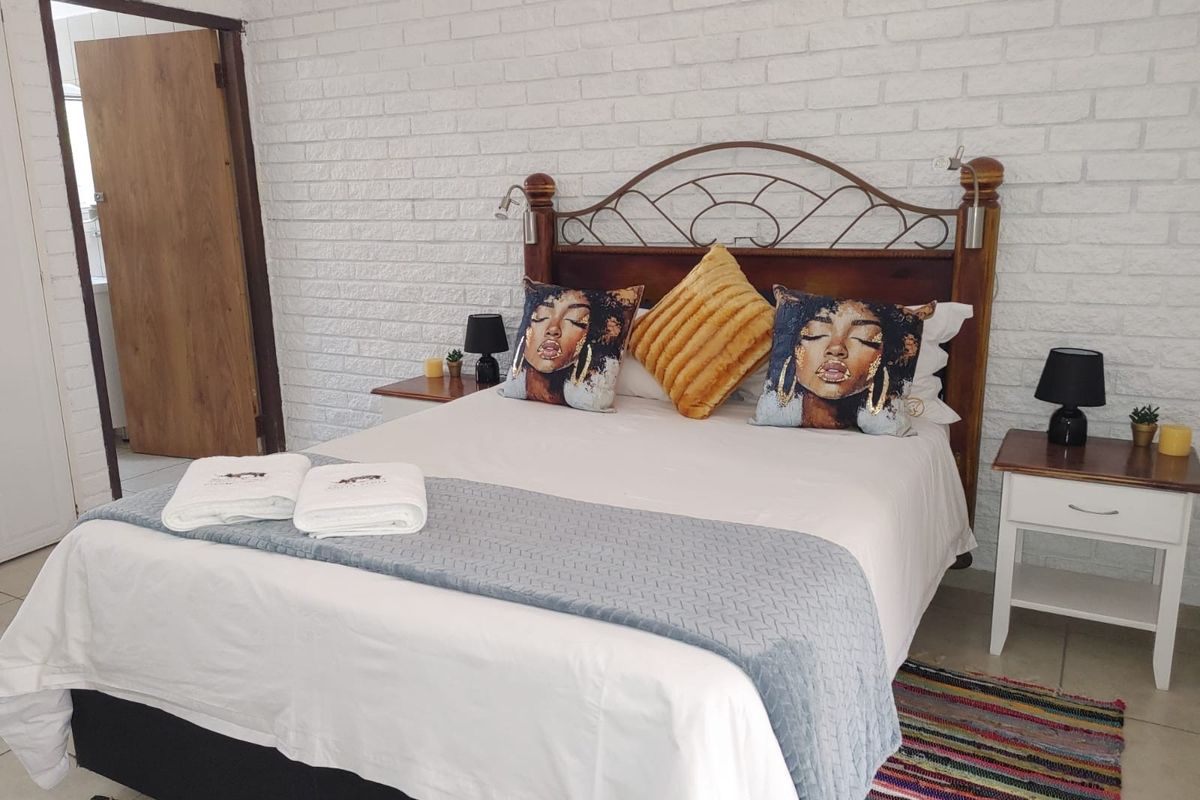 A bedroom featuring a white painted exposed brick feature wall and tiled flooring.