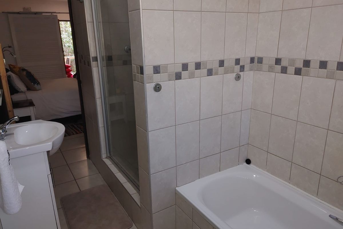 A functional bathroom featuring a shower enclosure, bathtub, and pedestal basin with neutral wall and floor tiling.