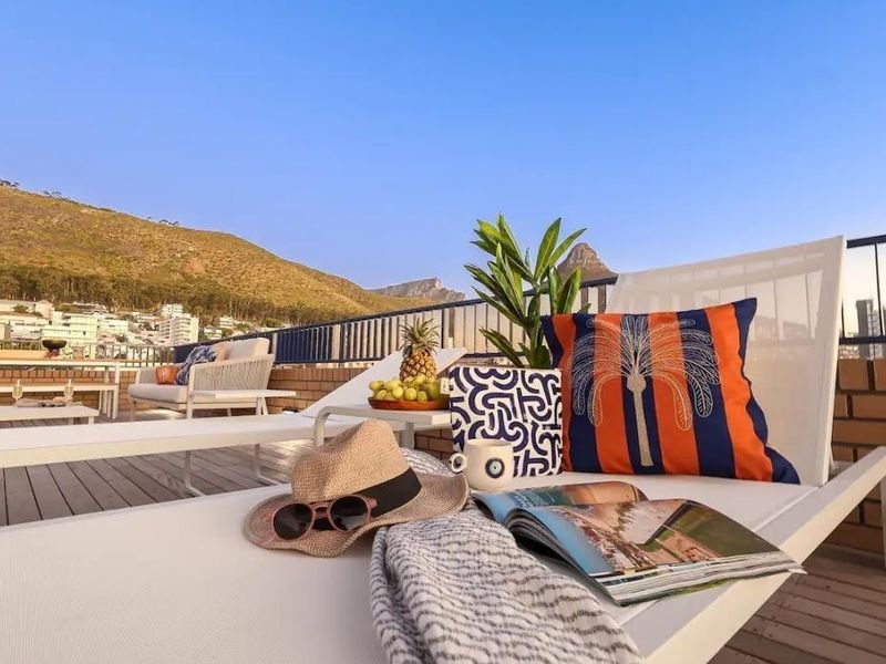 Spacious outdoor balcony featuring timber decking, brick parapet walls, and metal railings, offering scenic mountain and neighbourhood views.