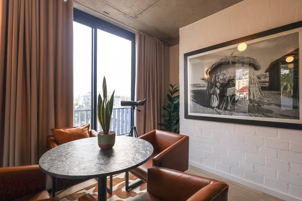 Modern living area featuring an exposed concrete ceiling, painted brick feature wall, and large sliding glass doors leading to a balcony.