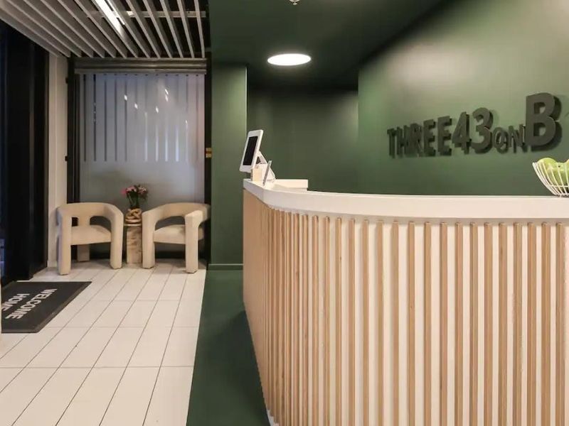 Modern reception area featuring a curved timber-slatted desk, dark green accent wall, and clean tiled flooring in a professional building entrance.