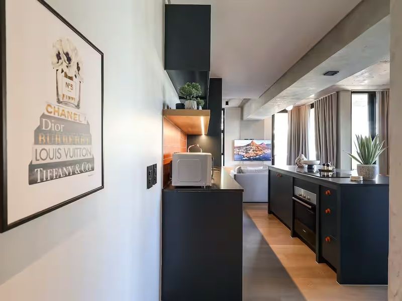 Modern open-plan living area featuring a sleek kitchen with dark cabinetry, integrated appliances, and exposed concrete ceilings, flowing into a comfortable lounge space.