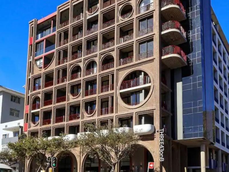 Modern multi-story apartment building featuring a distinctive brick facade with arched balconies, circular windows, and a ground-level commercial arcade.