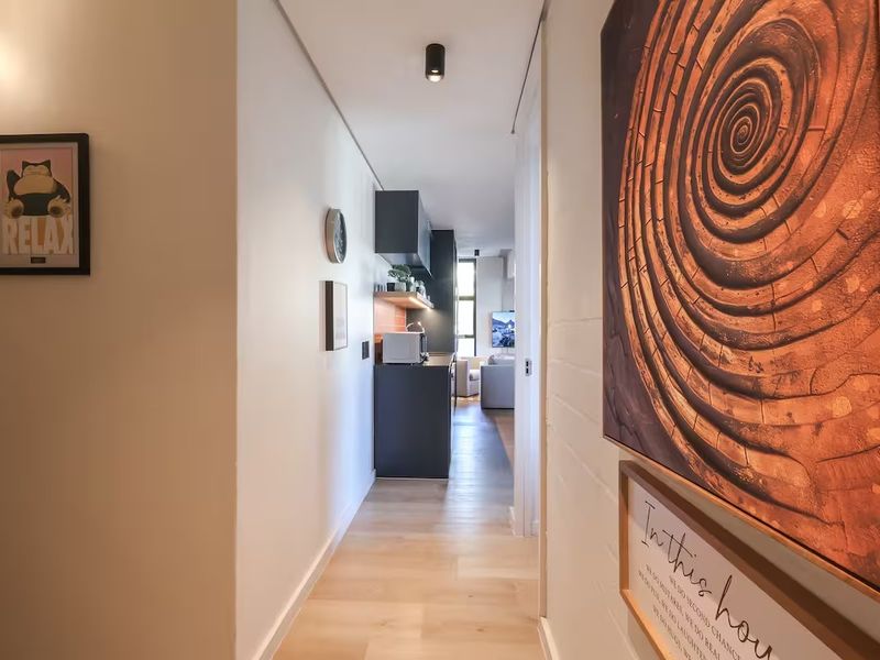 A bright, modern hallway featuring light wood-look flooring and recessed ceiling lighting, leading directly into an open-plan kitchen and living area.
