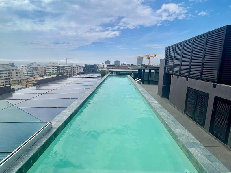 A modern rooftop lap pool featuring clean lines, tiled coping, and integrated lighting, set against an urban skyline backdrop.