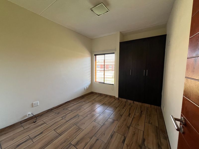 A clean, empty bedroom featuring wood-look tile flooring, a dark built-in wardrobe, and venetian blinds, offering a neutral space ready for personalization.