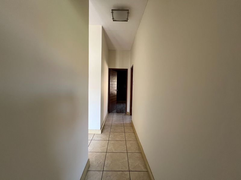 A clean, neutral hallway featuring tiled flooring and a flush mount ceiling light, providing access to adjacent rooms.
