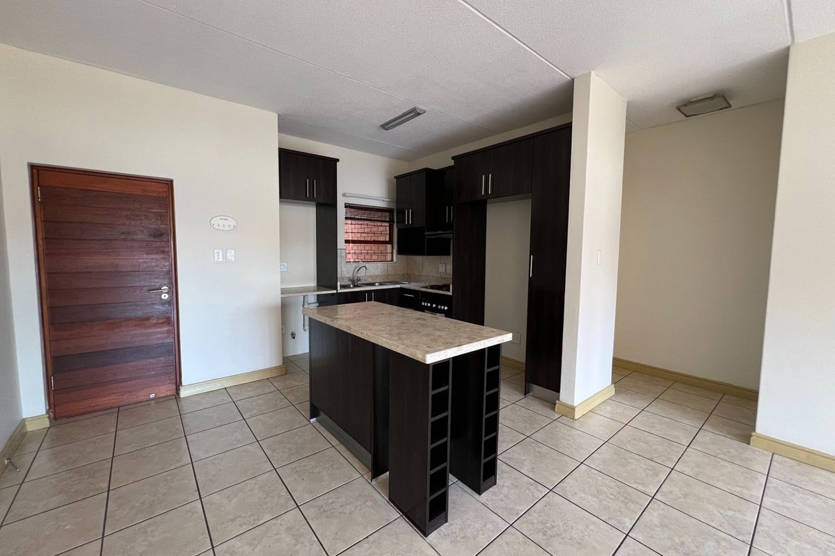 An open-plan kitchen featuring dark wood cabinetry, a central island with stone countertop, ceramic tiled flooring, and integrated cooking appliances.