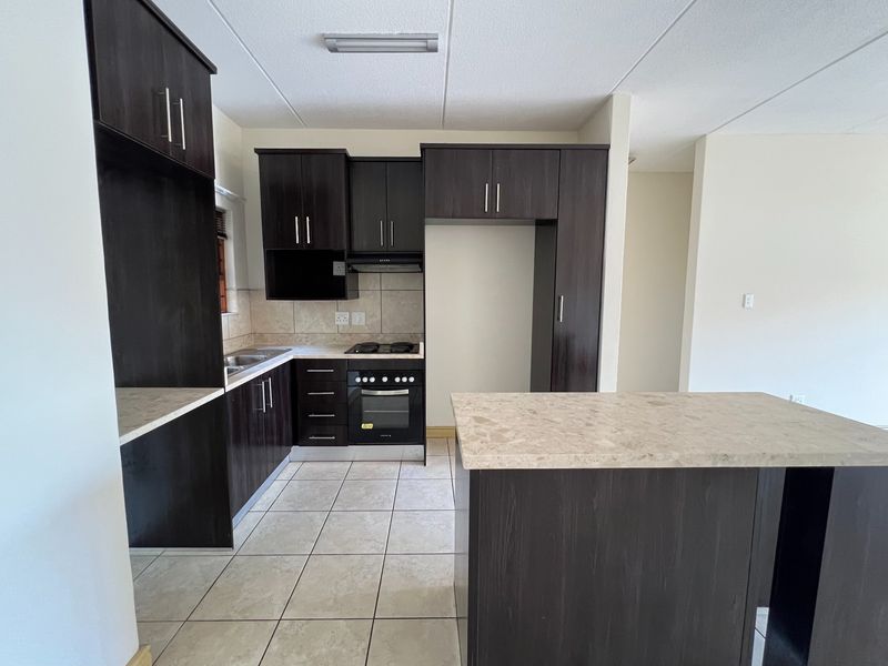 A clean, modern kitchen featuring dark wood cabinetry, stone-look countertops, a built-in oven with gas hob, and a functional kitchen island.