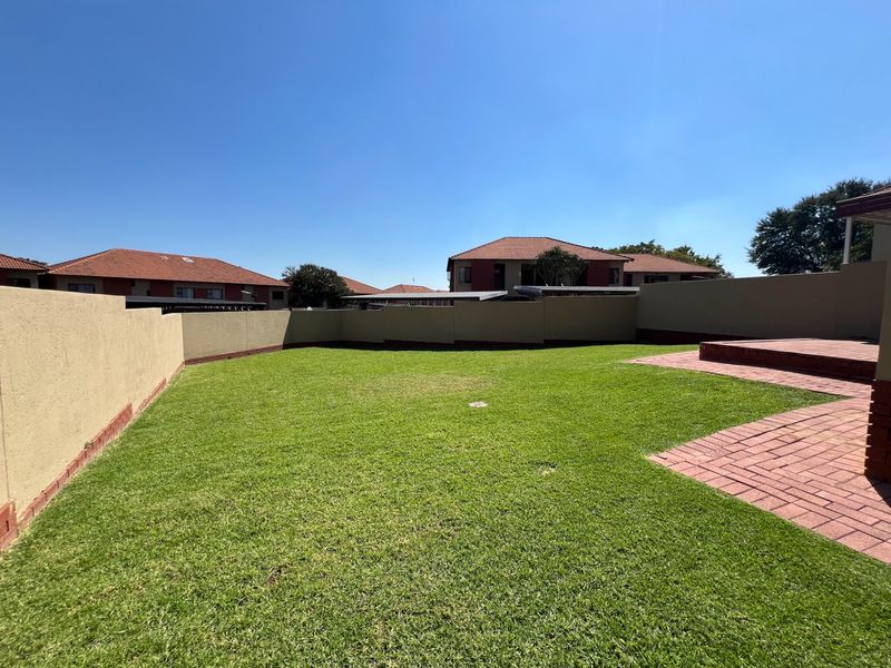 A private rear garden featuring a well-maintained lawn, perimeter boundary walls, and brick-paved patio area.
