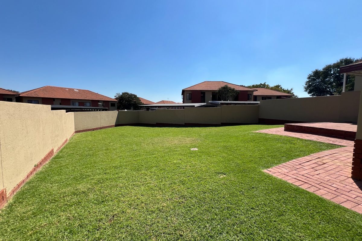 A private rear garden featuring a well-maintained lawn, perimeter boundary walls, and brick-paved patio area.