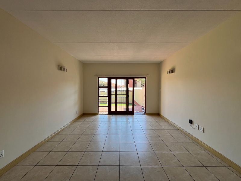 A spacious, empty living room featuring neutral tiled flooring and a sliding glass door that provides direct access to the rear outdoor area.