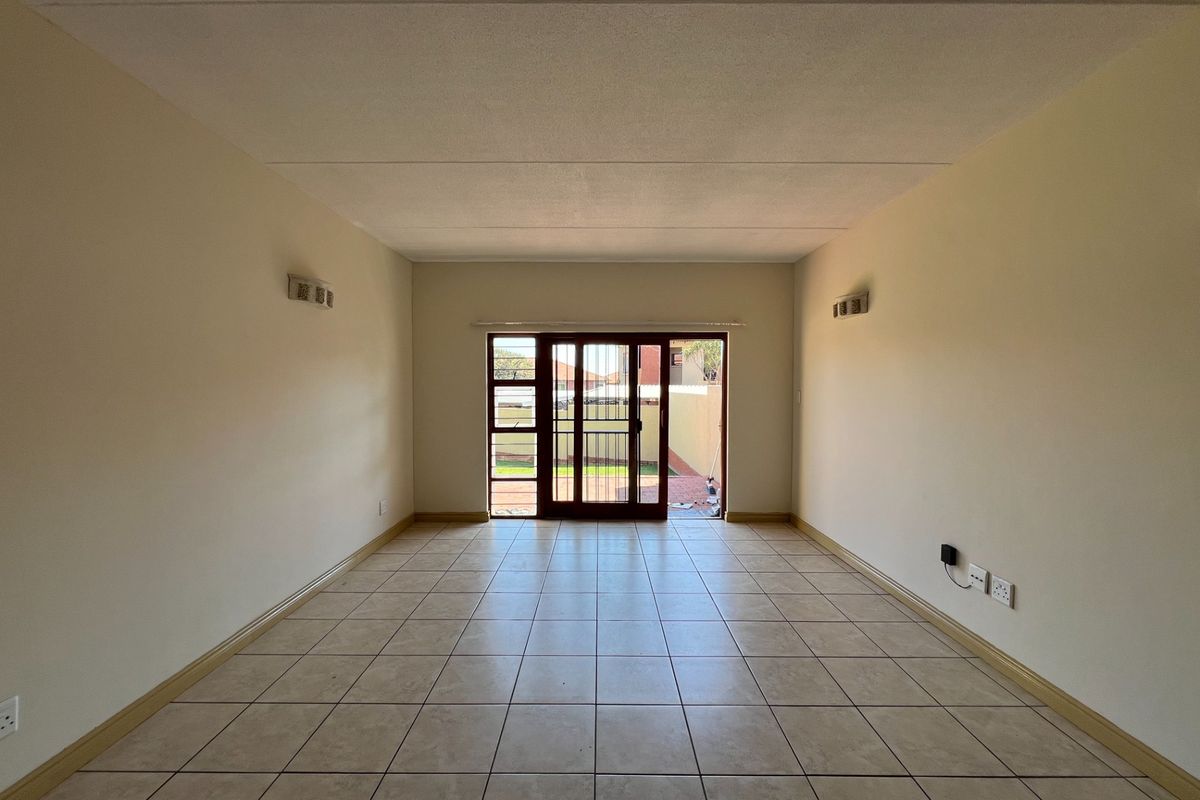 A spacious, empty living room featuring neutral tiled flooring and a sliding glass door that provides direct access to the rear outdoor area.