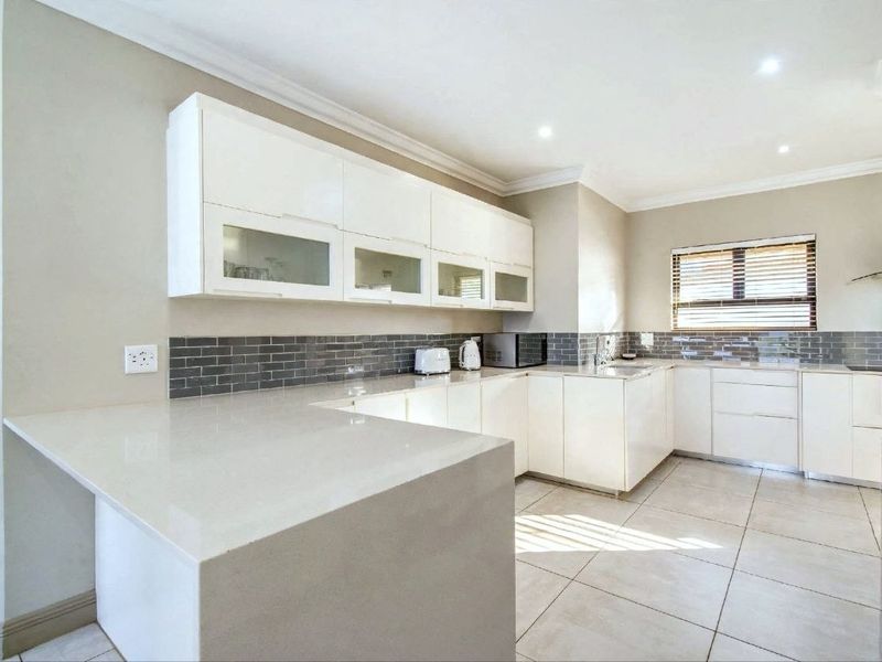 Modern kitchen featuring white cabinetry, quartz countertops, a grey subway tile backsplash, and neutral tile flooring with ample natural light.
