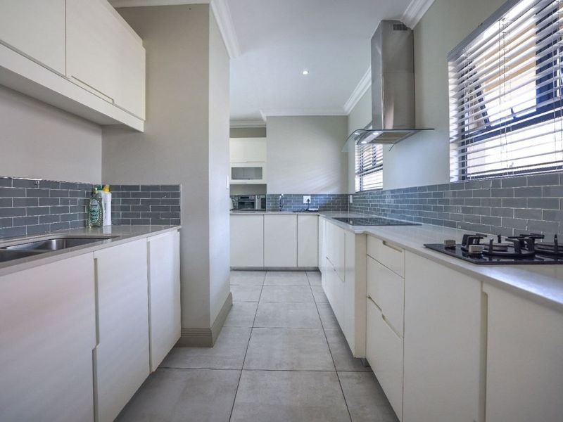 Modern galley-style kitchen featuring white cabinetry, stone countertops, grey subway tile backsplash, stainless steel extractor fan, and gas hob.
