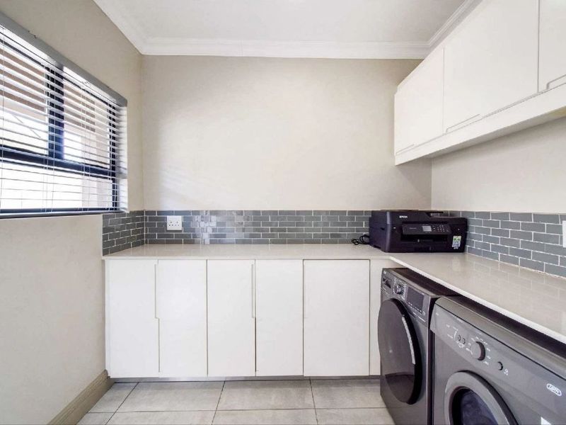 A clean and functional laundry room featuring white built-in cabinetry, stone countertops, grey subway tile backsplash, and tiled flooring.