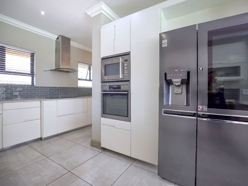 Modern kitchen featuring sleek white cabinetry, subway tile backsplash, built-in oven and microwave, stainless steel extractor fan, and neutral tiled flooring.