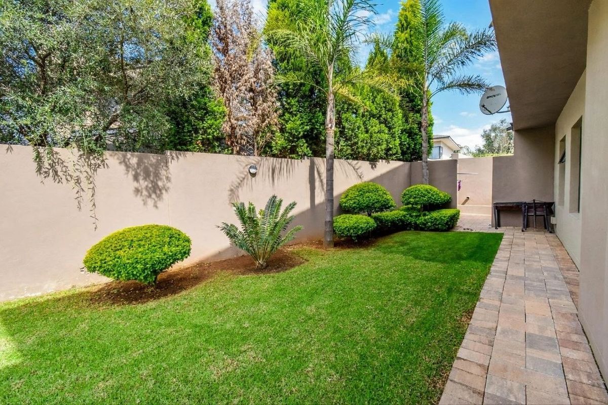 A well-maintained rear garden featuring a manicured lawn, shaped shrubbery, and a paved walkway along the side of the property.