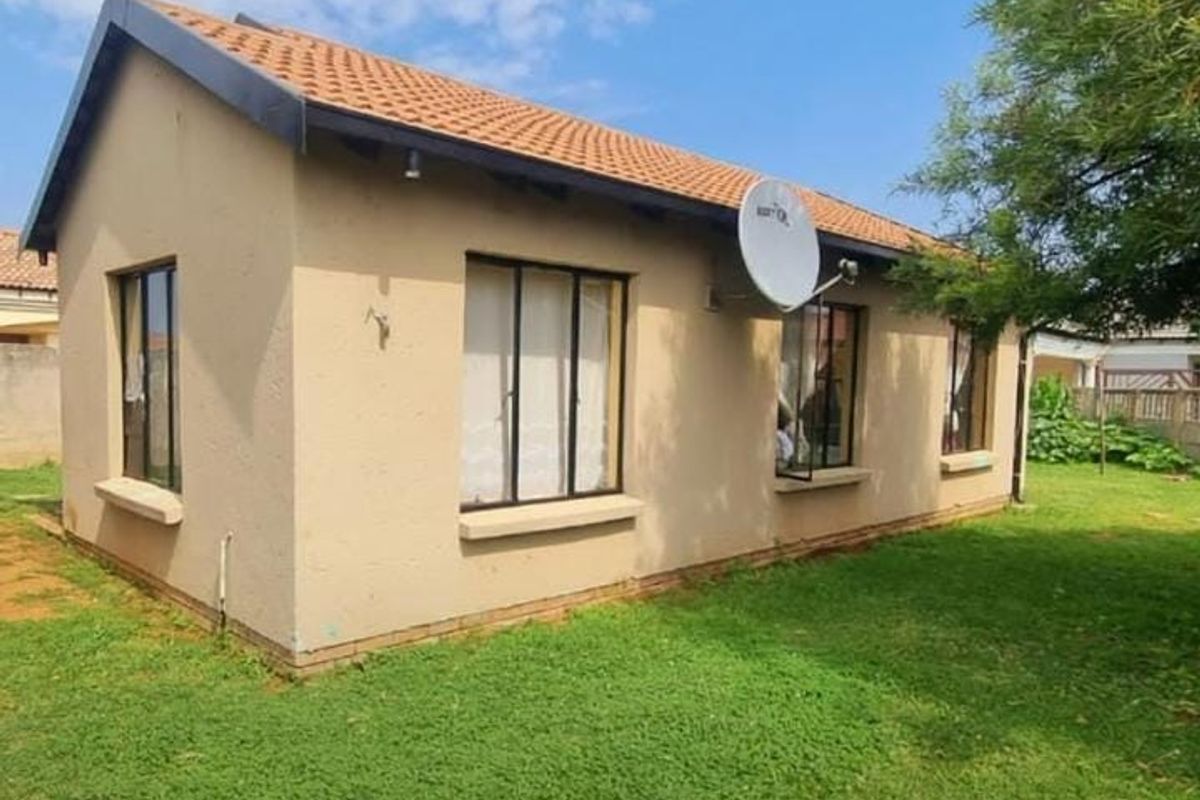 A view of the rear exterior of the house featuring plastered walls, terracotta roof tiles, and aluminium window frames set within a garden area.