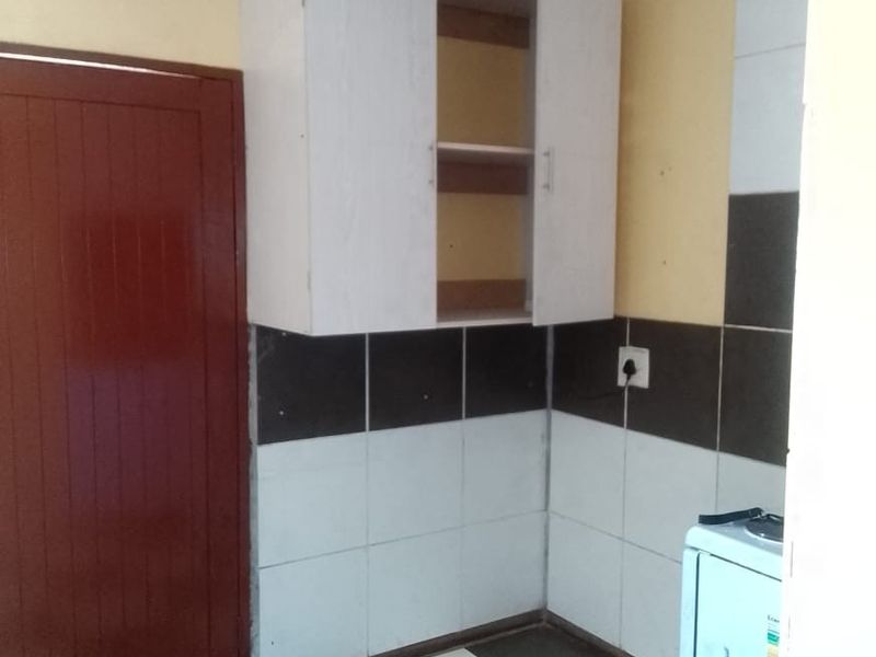 A small kitchen area featuring tiled flooring, a tiled splashback, and wall-mounted cabinetry, currently in need of cosmetic updates and repairs.