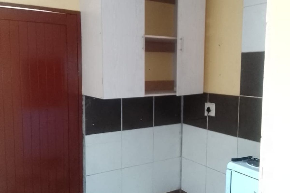 A small kitchen area featuring tiled flooring, a tiled splashback, and wall-mounted cabinetry, currently in need of cosmetic updates and repairs.