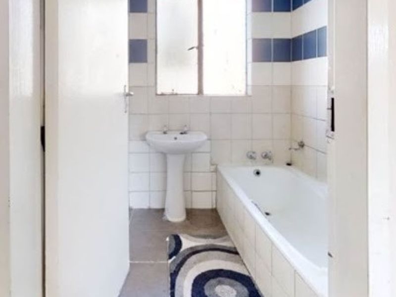 A functional bathroom featuring a pedestal basin, built-in bathtub, and tiled finishes, offering a blank canvas for modern renovation and design updates.