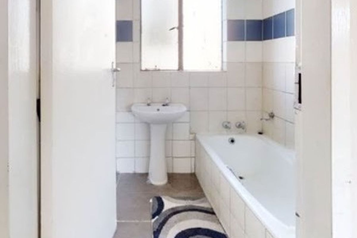 A functional bathroom featuring a pedestal basin, built-in bathtub, and tiled finishes, offering a blank canvas for modern renovation and design updates.