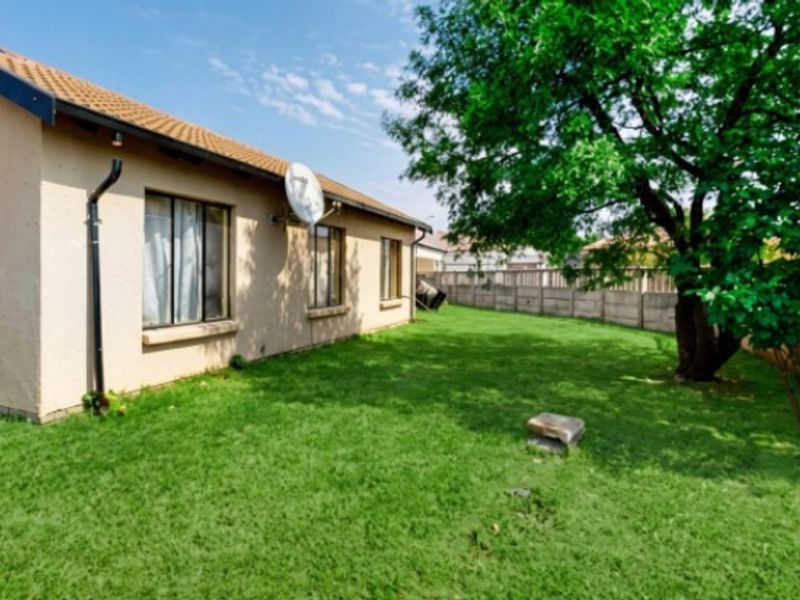 A view of the rear exterior of the house featuring a lawn, mature tree, and precast concrete boundary wall.