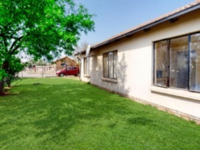 A view of the rear exterior of the house featuring a well-maintained lawn, plastered walls, and aluminium window frames.