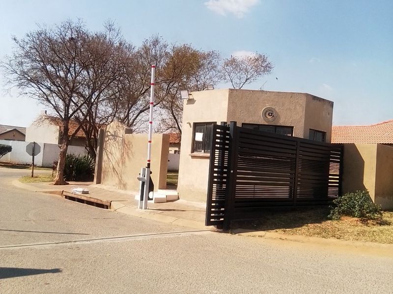 A view of the residential estate entrance featuring a security guard house, automated boom gate, and metal sliding security gate.