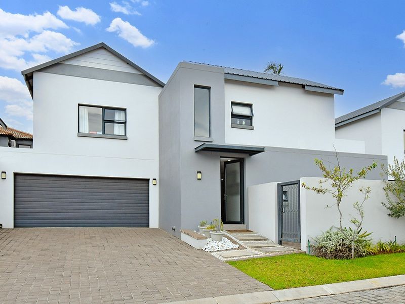 Modern double-story residential home featuring a paved driveway, integrated double garage, and a clean, contemporary facade with neutral grey and white finishes.